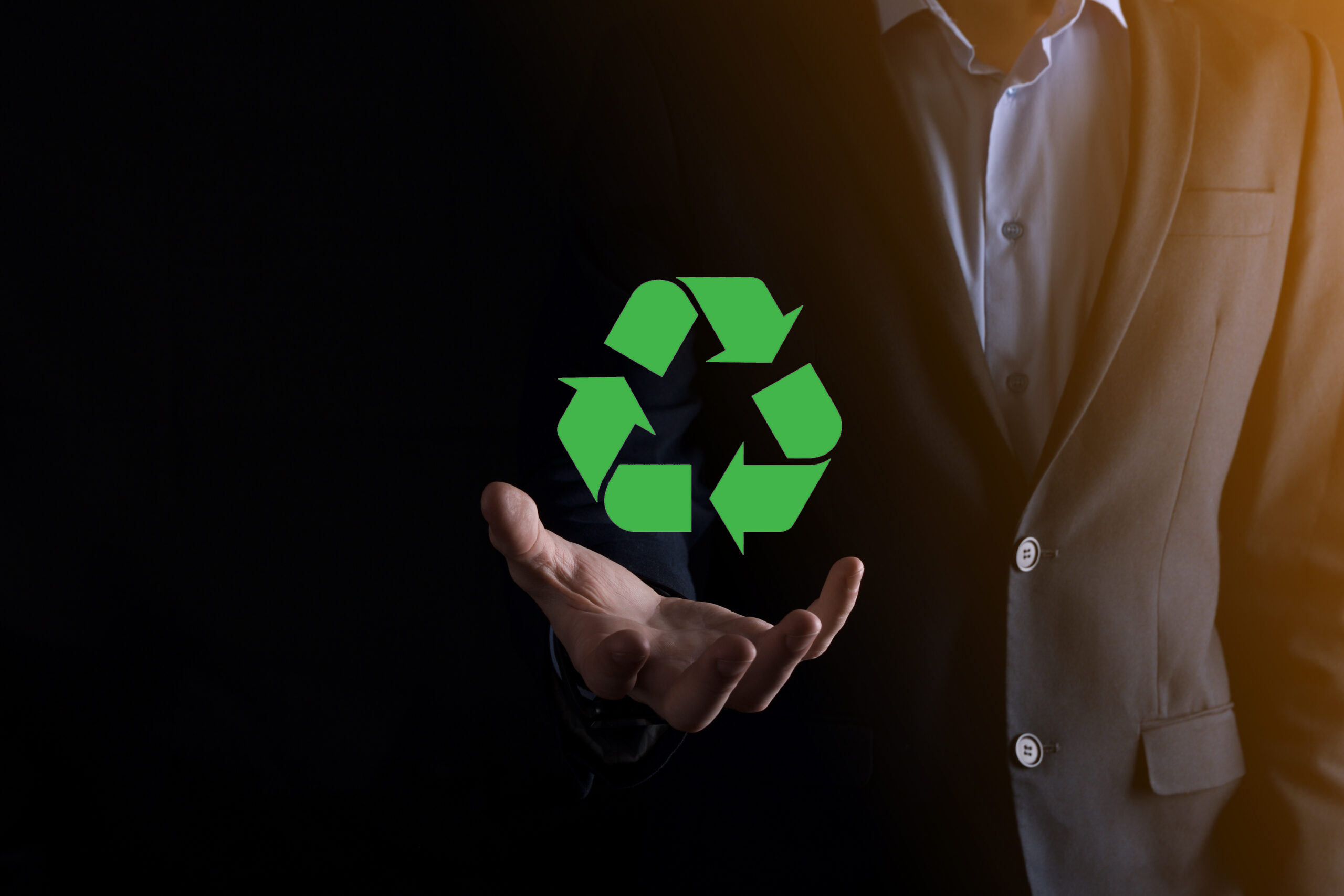businessman in suit over dark background holds an recycling icon, sign in his hands. ecology, environment and conservation concept. neon red blue light